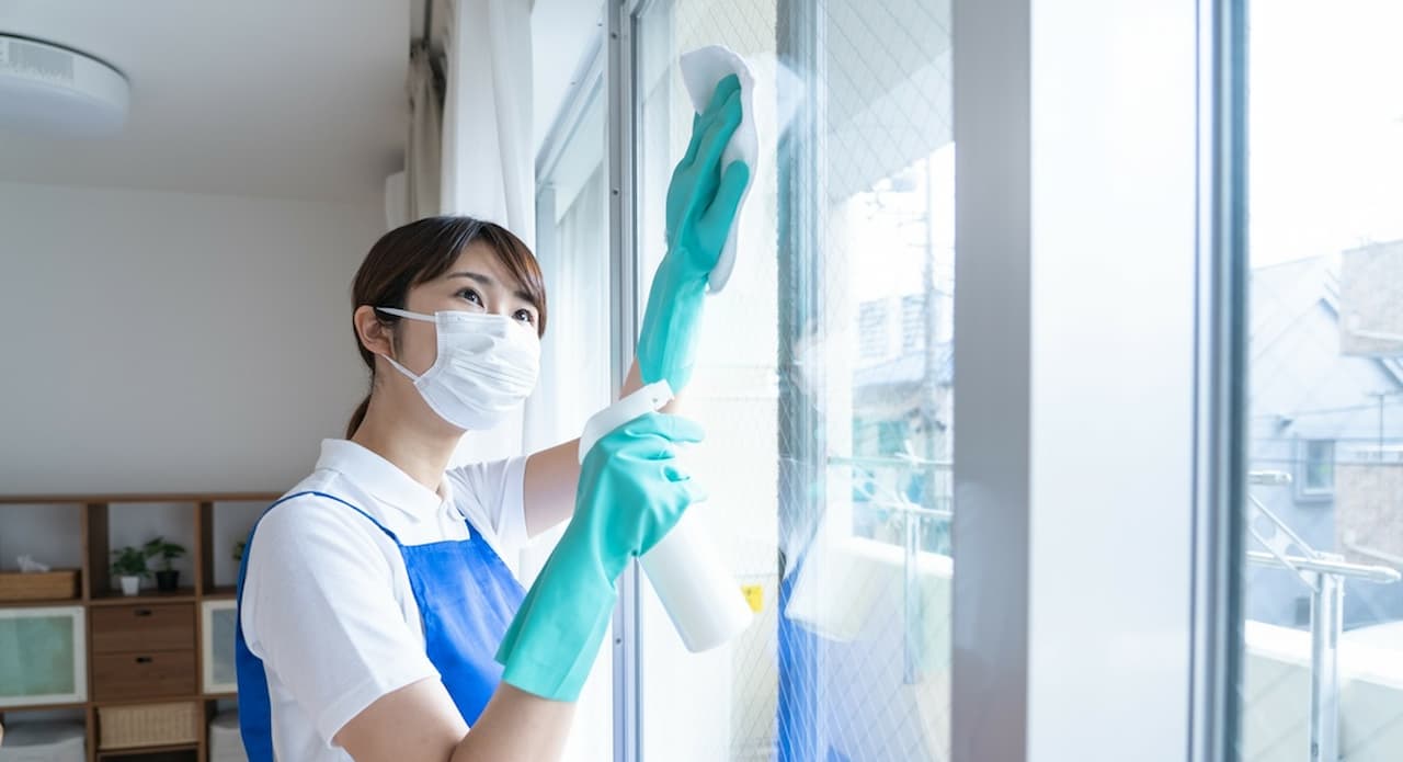 マスクとゴム手袋をして窓の掃除をする人