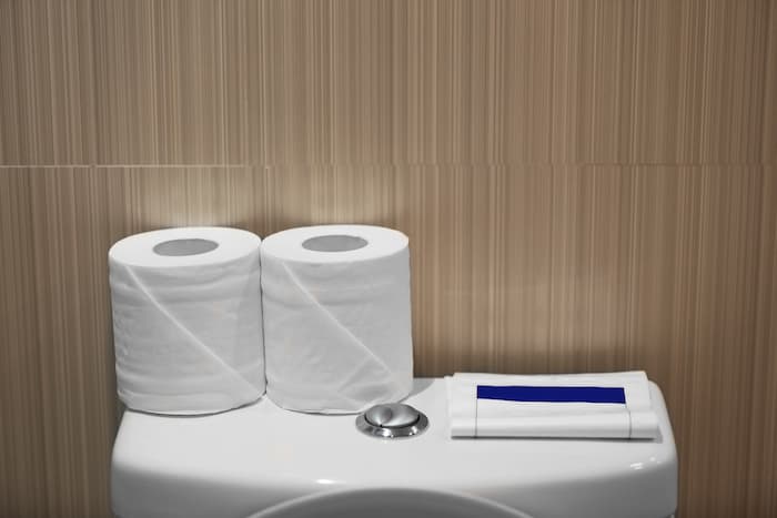 個室トイレの給水タンクの上にトイレットペーパーとエチケット袋が置かれている